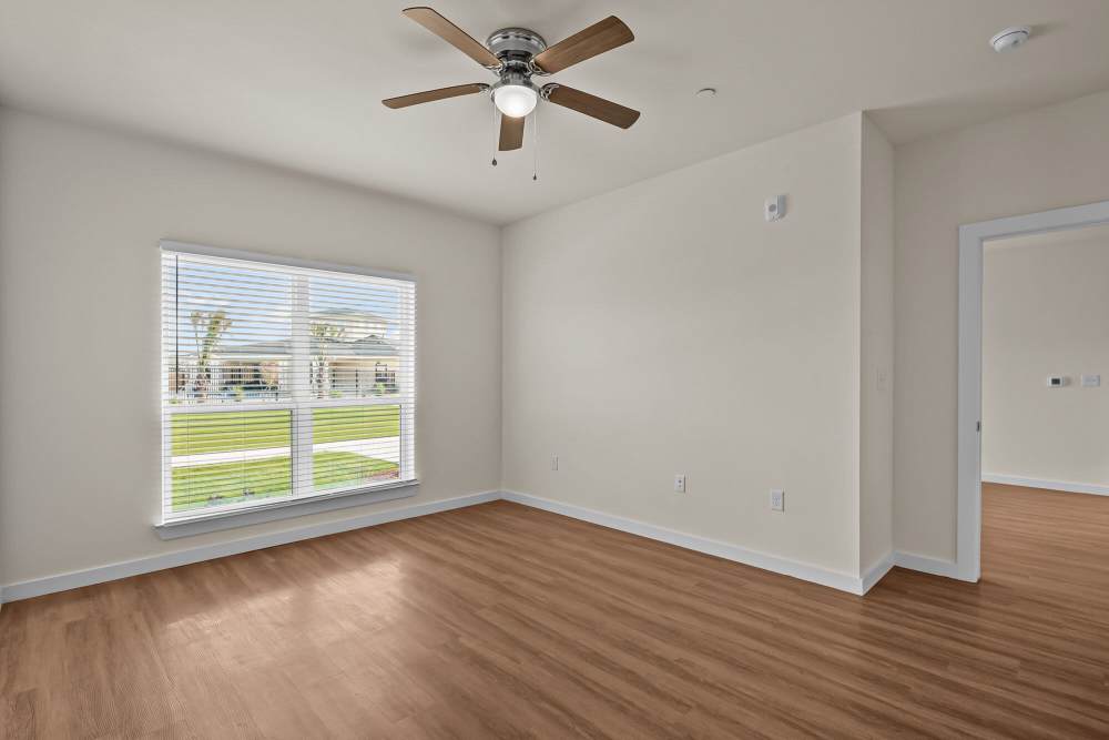 Bright living room with wood-style flooring and ceiling fan, large window with blinds, open layout at Springwood at Aliana in Richmond, Texas