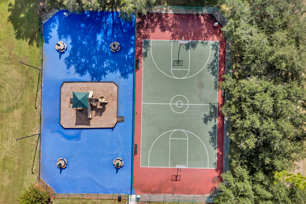 Aerial view of playground and basketball court surrounded by green grass and trees at Carlton Arms Of Winter Haven in Winter Haven, Florida