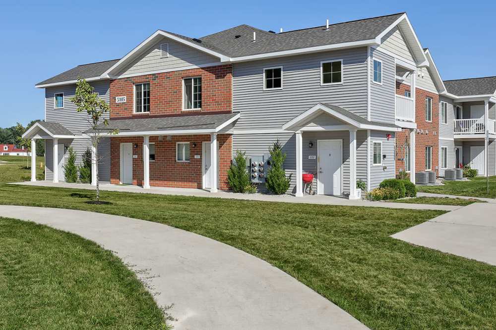 Two-story apartment buildings with green lawns and walkways, featuring balconies and a gated entrance at Brookside Commons in Traverse City, Michigan