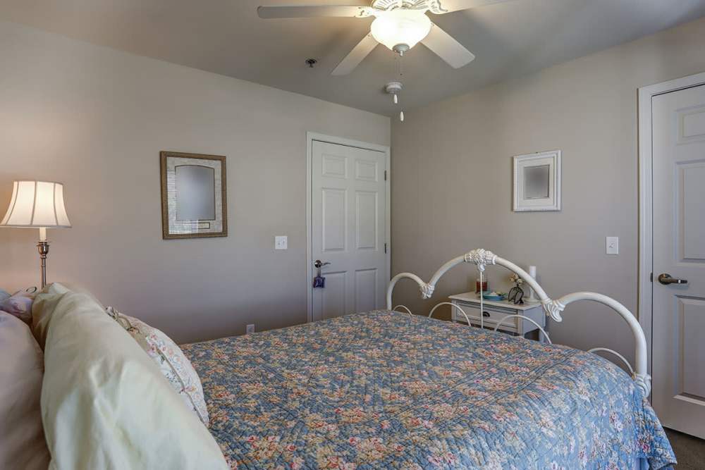 Cozy bedroom with floral bedding, white metal bed frame, lamp, and mirror on the wall at Brookside Commons in Traverse City, Michigan