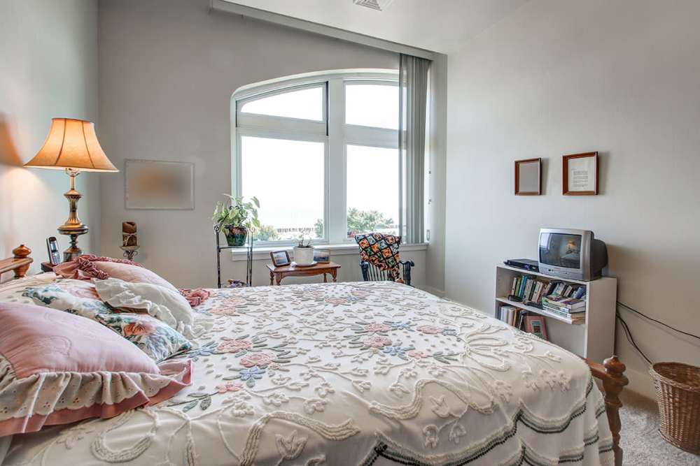 Cozy bedroom with large windows, floral bedding, lamp, and small bookshelf with TV at Lloyd House I in Menominee, Michigan