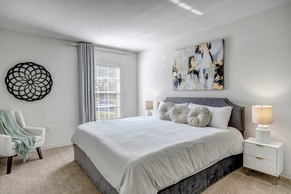 Comfortable bedroom with king size bed, side table lamp, wall art and carpet flooring at Carlton Arms Of North Lakeland in Lakeland, Florida