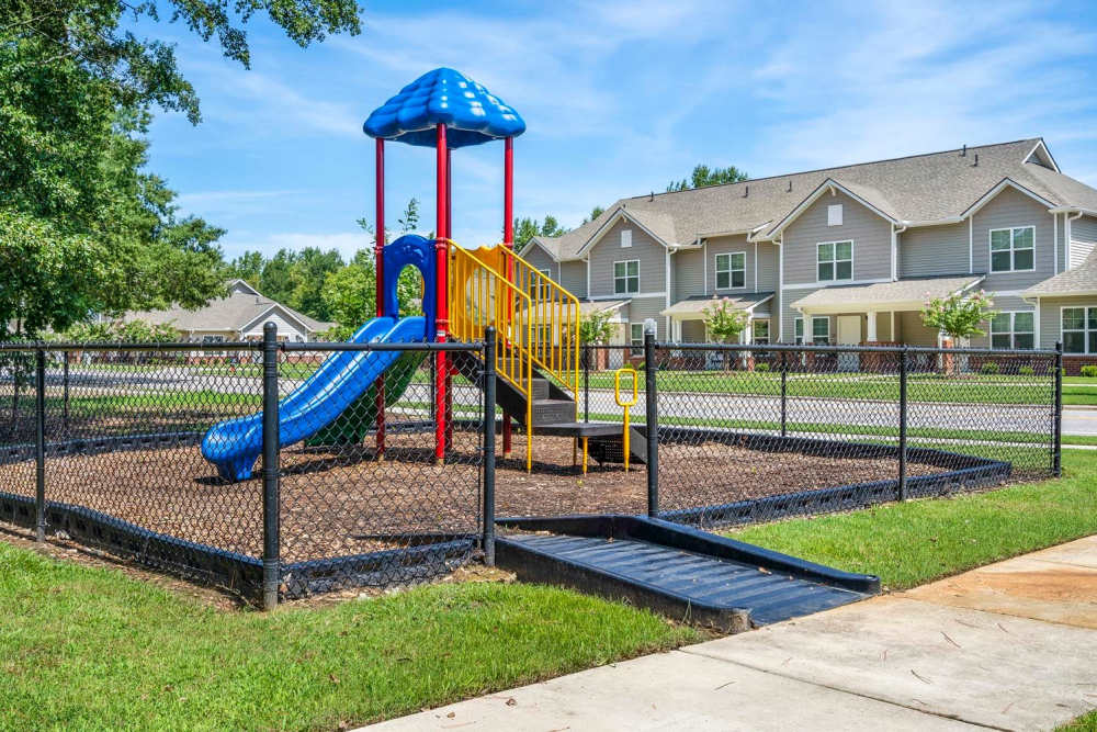 Colorful playground with slide and climbing structure, surrounded by a fenced area and green grass at Ravenwood Crossing in Rocky Mount, North Carolina