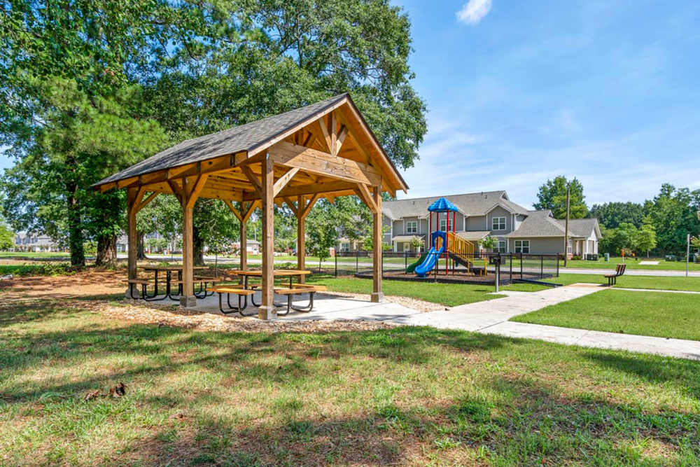 Wooden gazebo with picnic tables near playground and grassy area in a sunny apartment community at Ravenwood Crossing in Rocky Mount, North Carolina