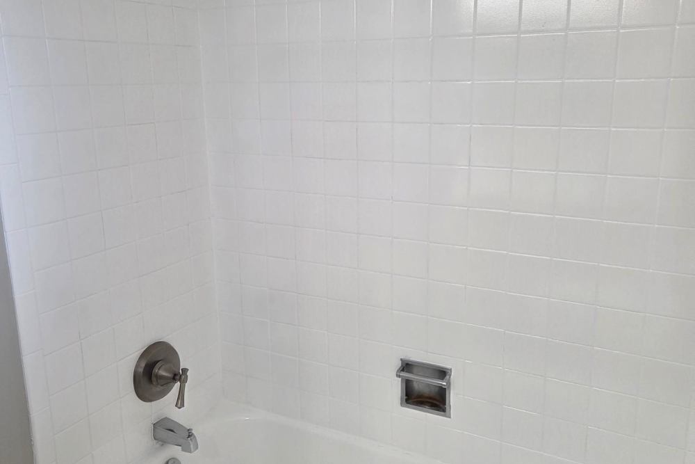 White bathtub with tiled shower walls, chrome fixtures, and built-in soap holder at Boulder Crescent in Colorado Springs, Colorado