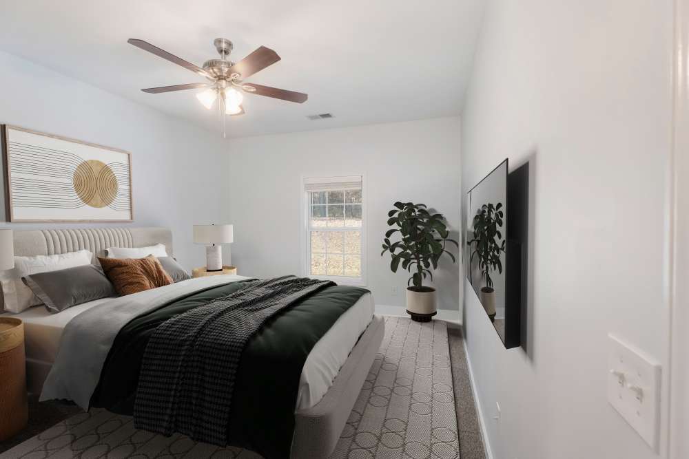 Cozy bedroom with a ceiling fan, large window, and stylish decor elements at Crystal Lake & Kingsley Apartments and Townhomes in Fayetteville, North Carolina