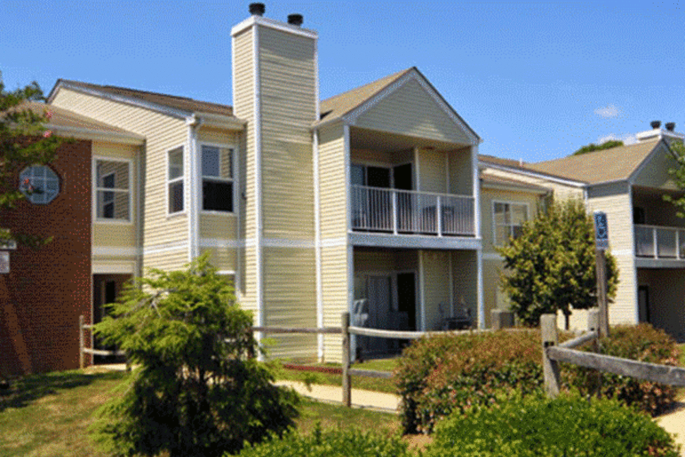 Two-story apartment building with balconies, surrounded by greenery and a wooden fence at Spring Valley Apartments in Lexington Park, Maryland
