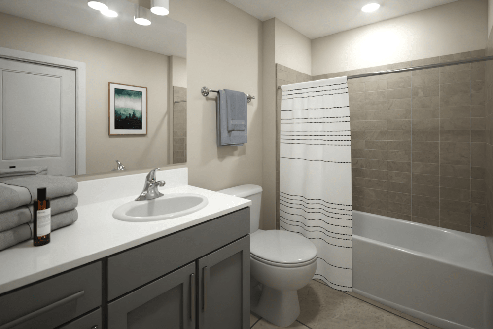 Apartment bathroom at The Exchange at Spring Hill Station with modern vanity, gray cabinetry, and tiled tub surround