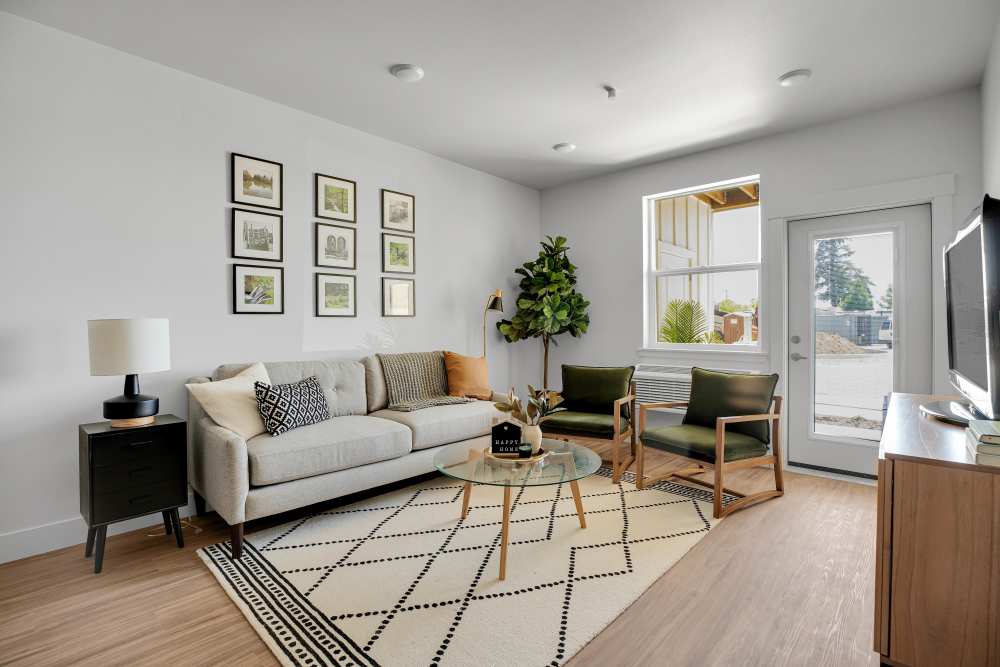 Bright living room with wood-style flooring, modern furniture, and large windows for natural light at Tilian Point in Woodburn, Oregon