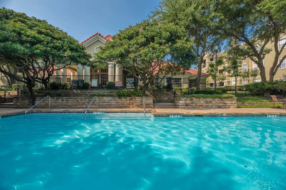 Clear blue swimming pool bordered by stone walls, trees, and a fenced clubhouse in the background at 530 Buckingham in Richardson, Texas
