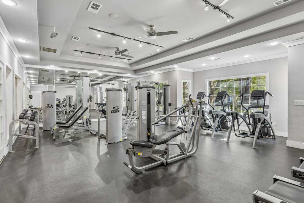 Modern community fitness center with treadmills, weight machines, benches, mirrors, and large windows at 530 Buckingham in Richardson, Texas