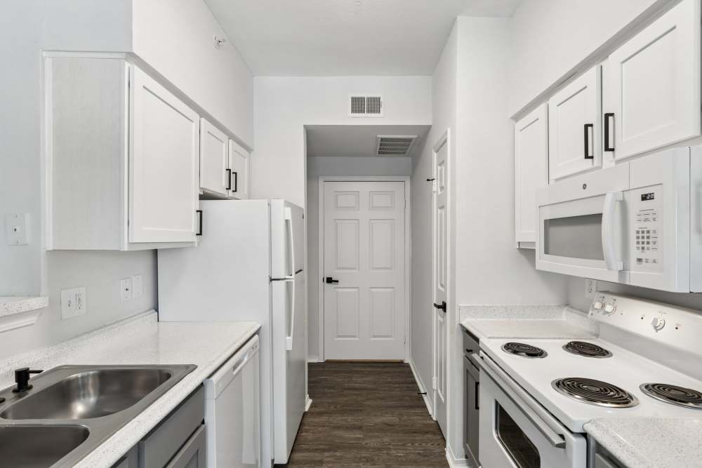 Galley kitchen opening to dining area, featuring white cabinets, black hardware, double sink, and window lighting at 530 Buckingham in Richardson, Texas