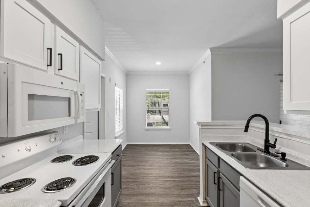 Narrow galley kitchen with white cabinets, electric range, microwave, refrigerator, double sink, and wood‑style flooring at 530 Buckingham in Richardson, Texas