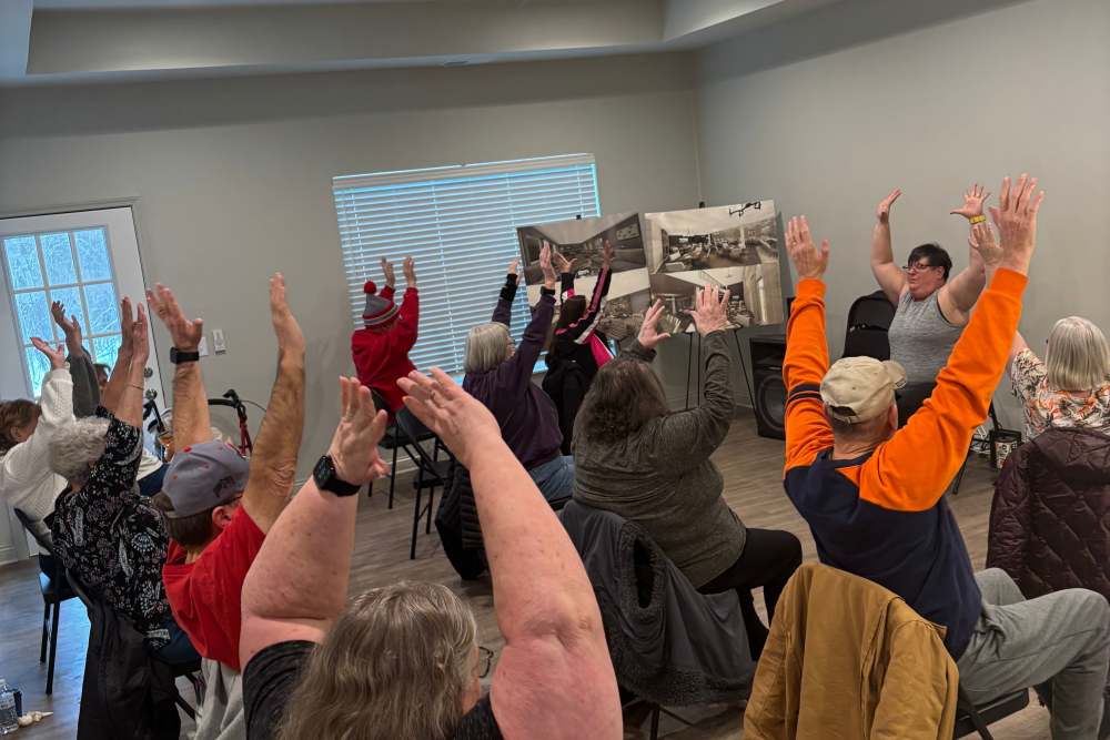 Group seated in chairs with arms raised during an indoor exercise or wellness class at Legacy Living Defiance in Defiance, Ohio  