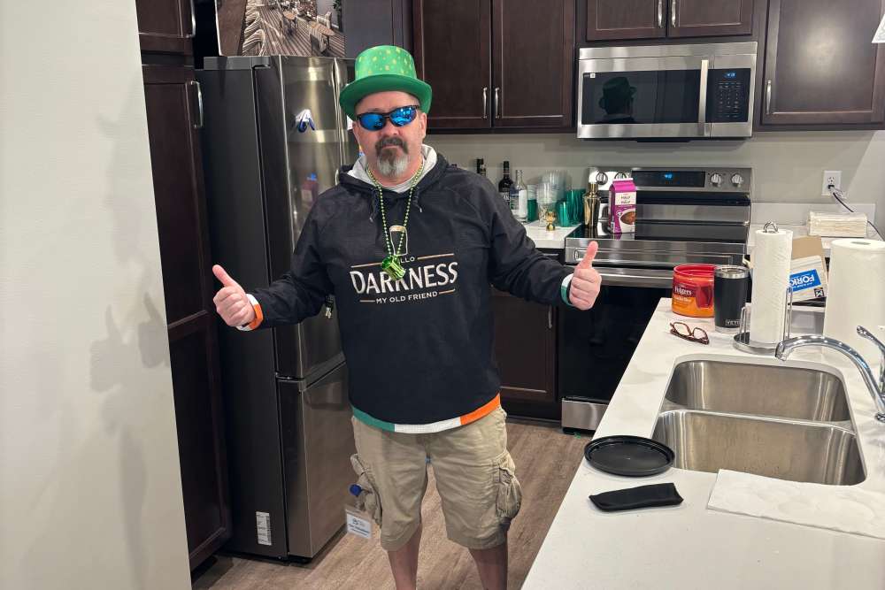 Person in a kitchen wearing a green hat and sunglasses, giving thumbs up next to a countertop and appliances at Legacy Living Defiance in Defiance, Ohio  