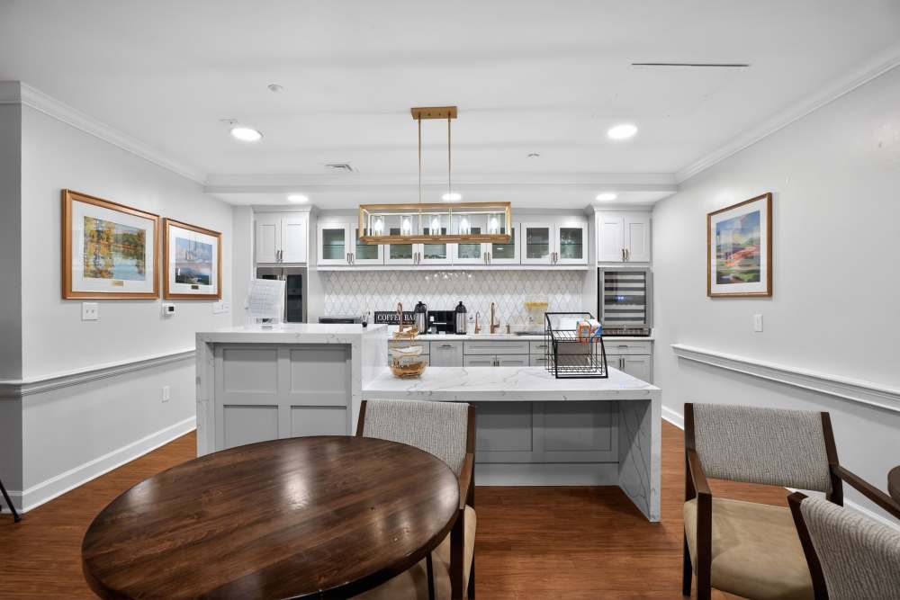 Modern beverage station with white cabinetry, quartz-style island counter, pendant lighting, and nearby café table with chairs at Glenncrest at Decatur in Decatur, Georgia