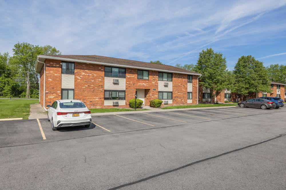 Brick apartment building with parking lot and cars in front under blue sky at Woodland Manor in Farmington, New York