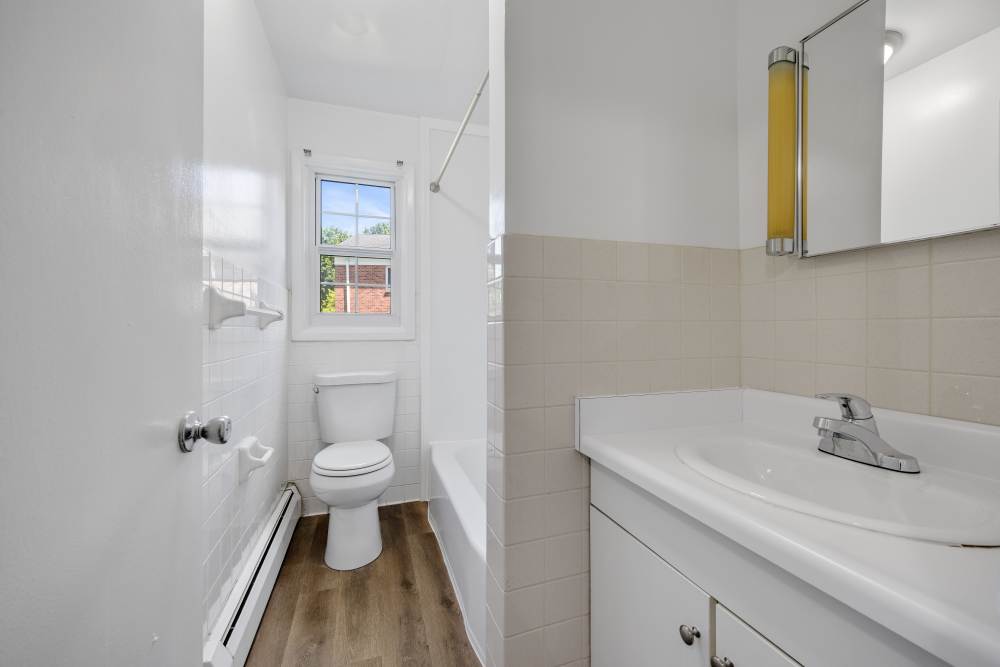 Narrow bathroom with toilet, tub, window, and sink vanity at Pittsford Village Estates in Pittsford, New York