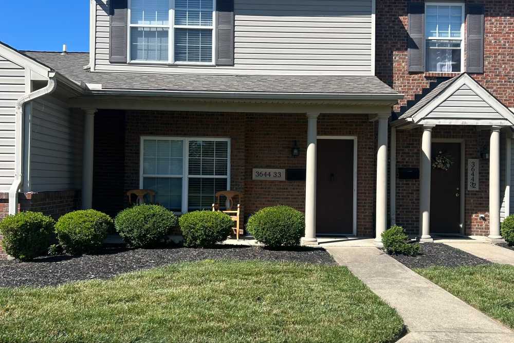 Front entrance of apartment with seating and landscaped shrubs at Whispering Wind Apartments & Townhomes in Newtown, Ohio
