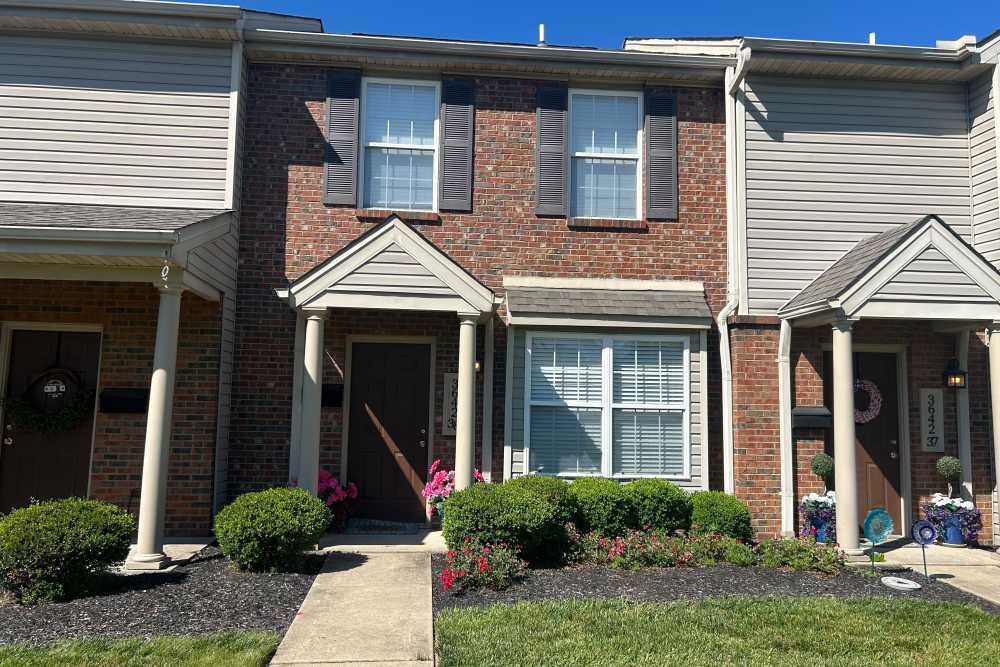 Brick townhouse exterior with landscaped shrubs at Whispering Wind Apartments & Townhomes in Newtown, Ohio