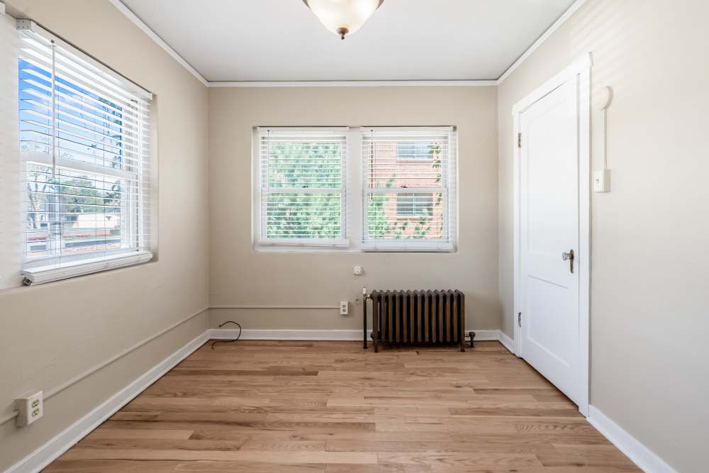 Empty bedroom with hardwood floors, two windows, radiator, and ceiling light in neutral tones at Cascade Park in Colorado Springs, Colorado