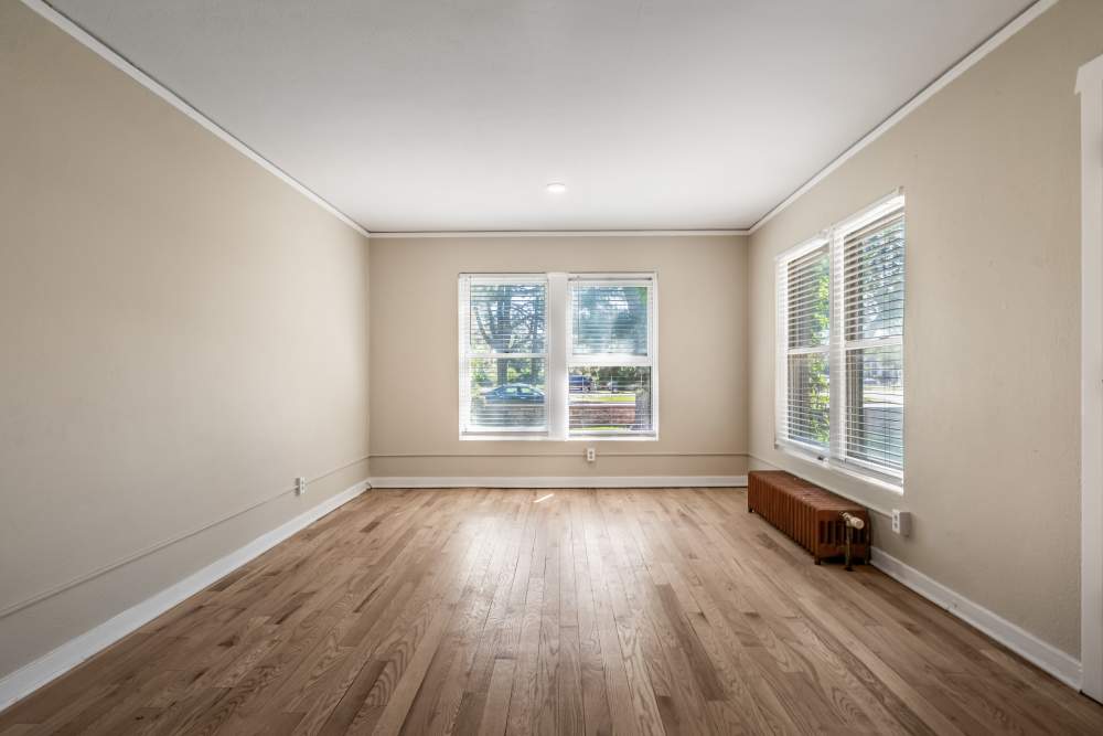 Spacious living area with wood floors, corner windows, radiator, and front entry door at Cascade Park in Colorado Springs, Colorado