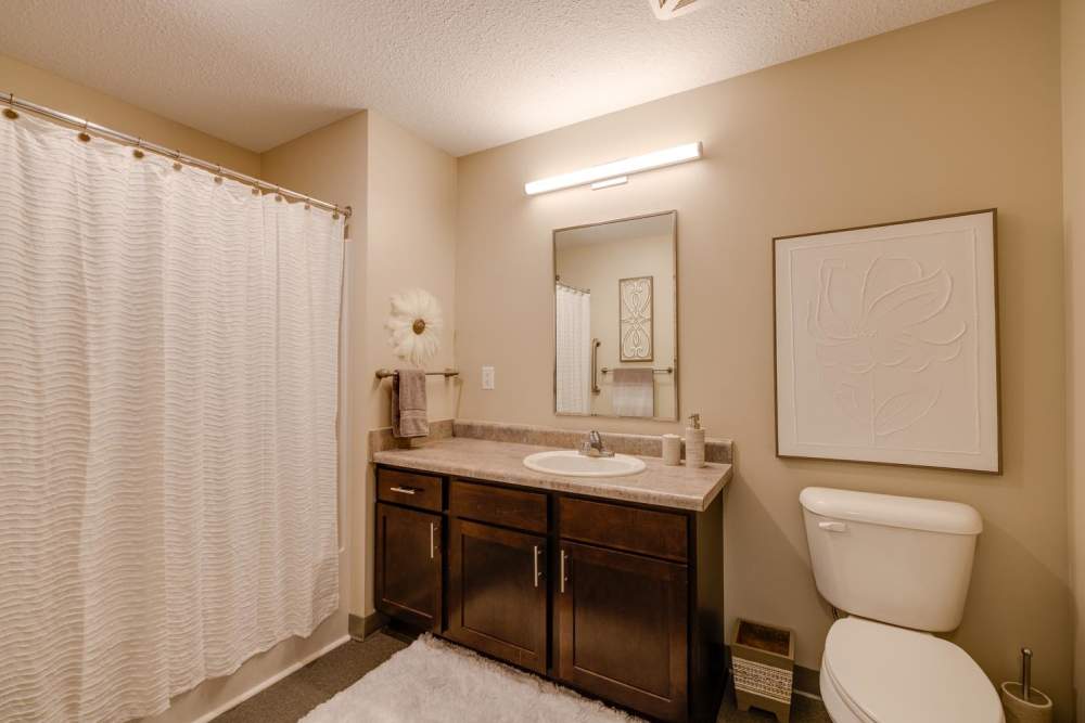Modern bathroom with dark wood cabinetry, large mirror, and white shower curtain at Johnston Crossing II in Johnston, Iowa