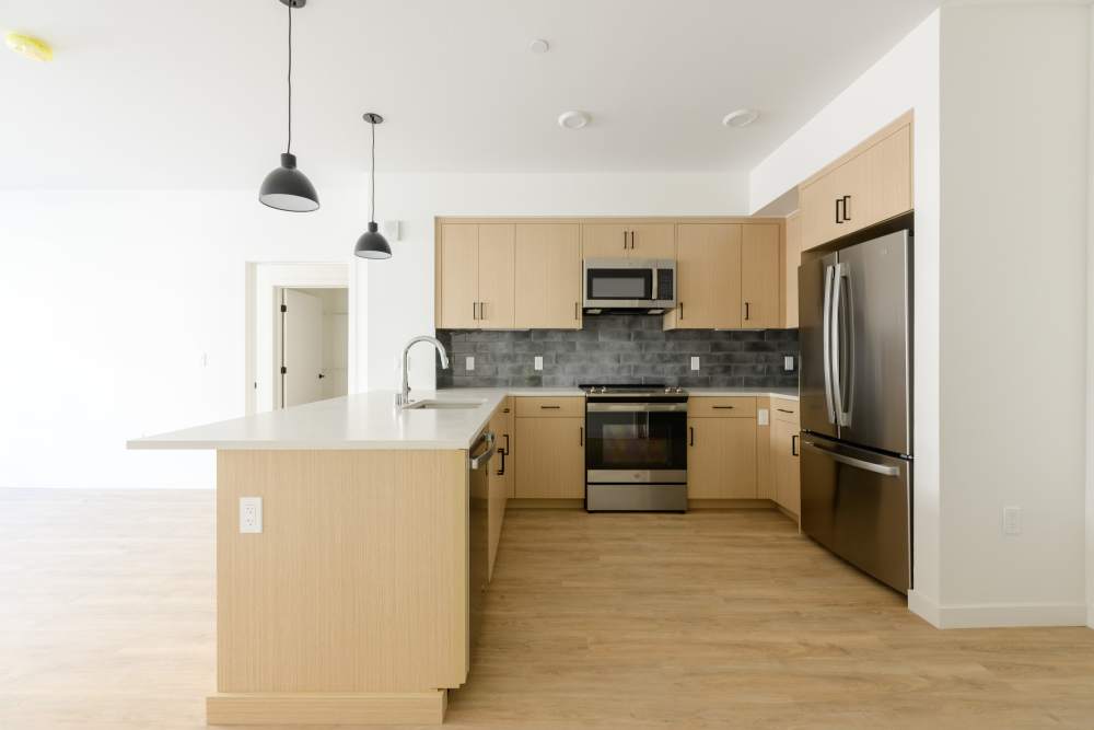 Modern kitchen with island, sink, pendant lights, wood cabinets, stainless appliances, and gray tile backsplash at Artisan Crossing in Belmont, California