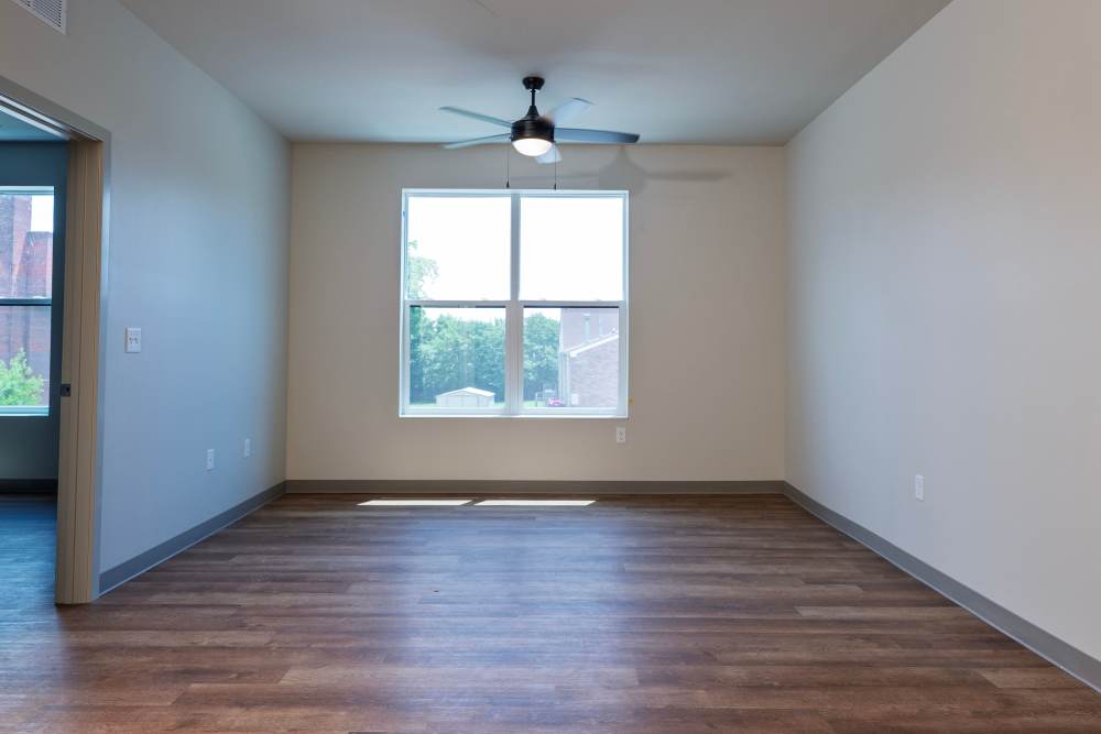 Living room with large window, ceiling fan, and wood floors at Monarch Station in Louisville, Kentucky