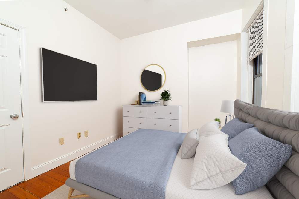 Minimal bedroom with upholstered bed, dresser, TV, and mirror at 71 Westland Apartments in Boston, Massachusetts
