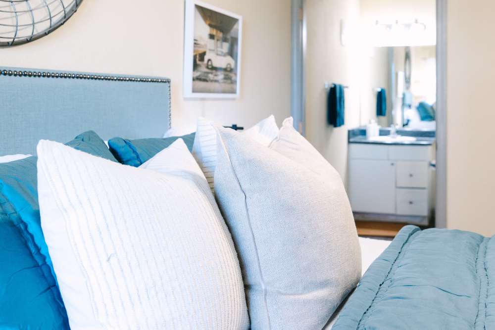 Bedroom with upholstered headboard, layered pillows, and view into ensuite bathroom at The Holly in Lubbock, Texas