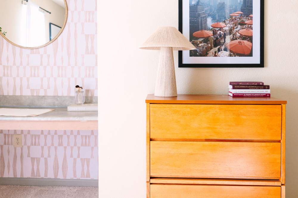 Bedroom with wood dresser, table lamp, wall art, and vanity area with round mirror at The Holly in Lubbock, Texas