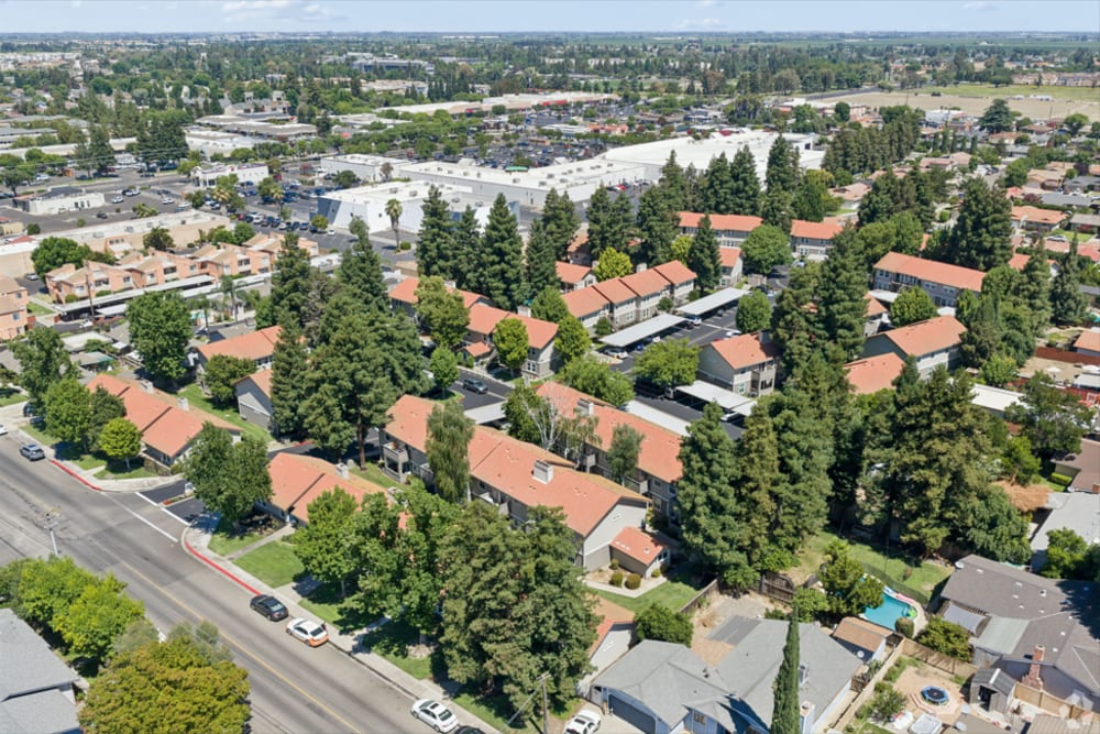 Aerial view of landscaped apartment community with tree-lined streets and nearby shops at Walnut Woods in Turlock, California