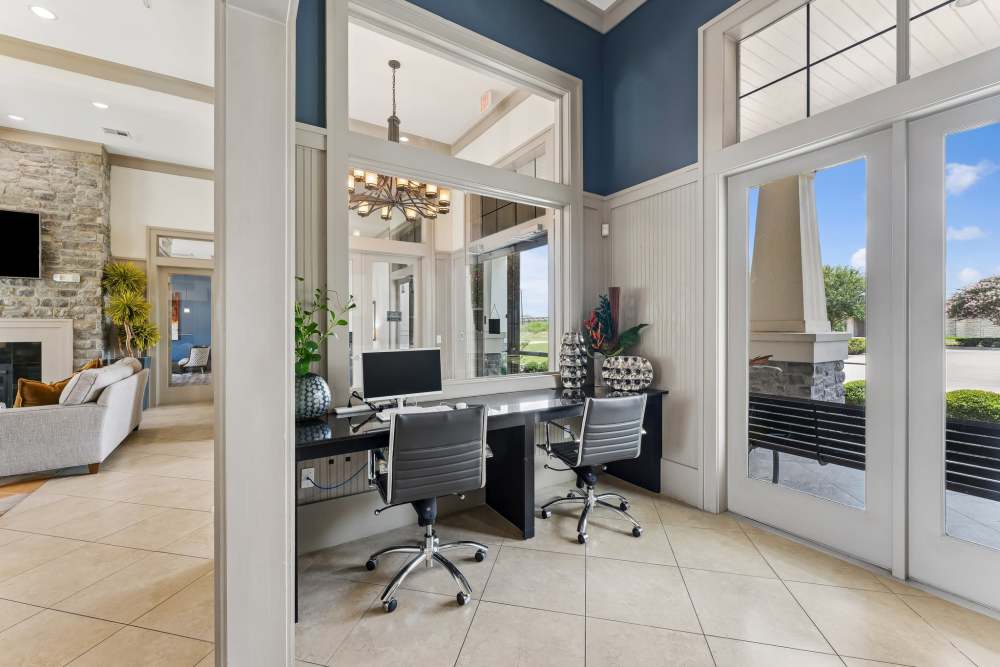 Bright office space with two desks, modern chairs, and large glass doors leading outside at Aria Victoria Apartments in Victoria, Texas