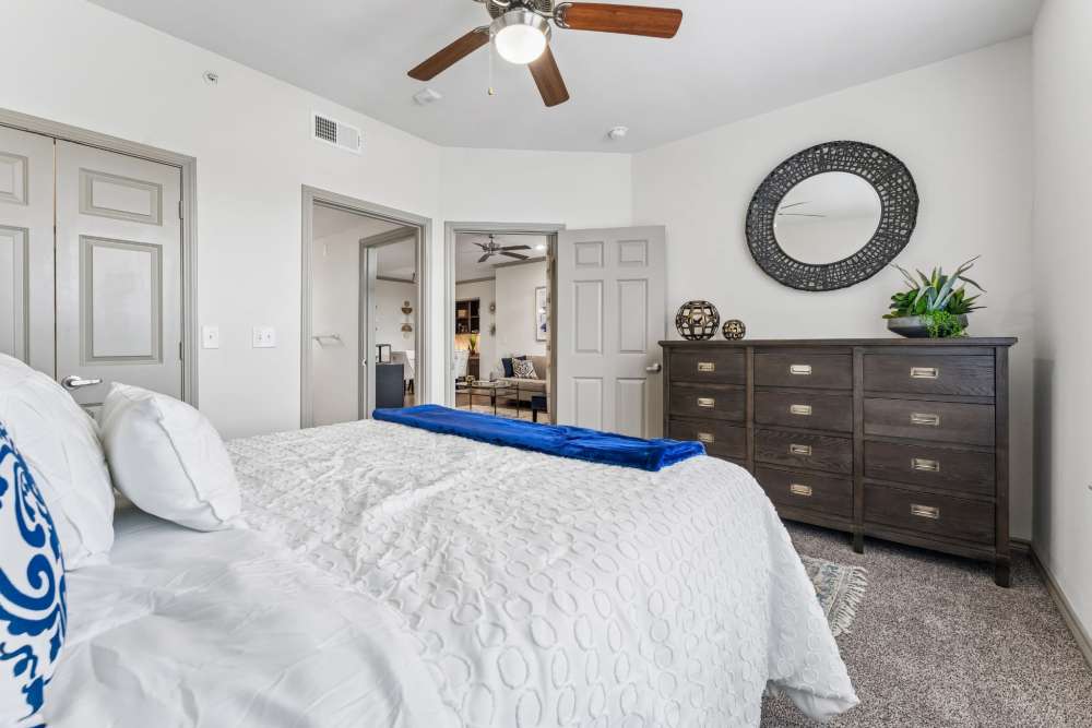Spacious bedroom with ceiling fan, hardwood flooring, and stylish dresser, featuring decorative plants and mirror at Aria Victoria Apartments in Victoria, Texas