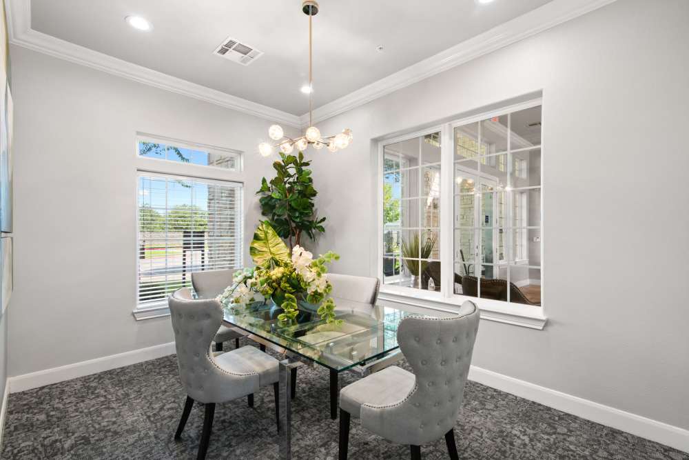 Elegant dining area with glass table, plush chairs, and decorative plants under natural light at Residence at Lake Jackson in Lake Jackson, Texas