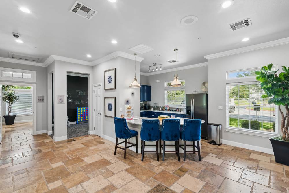 Bright community lounge with blue chairs, stone flooring, and large windows for natural light at Residence at Lake Jackson in Lake Jackson, Texas