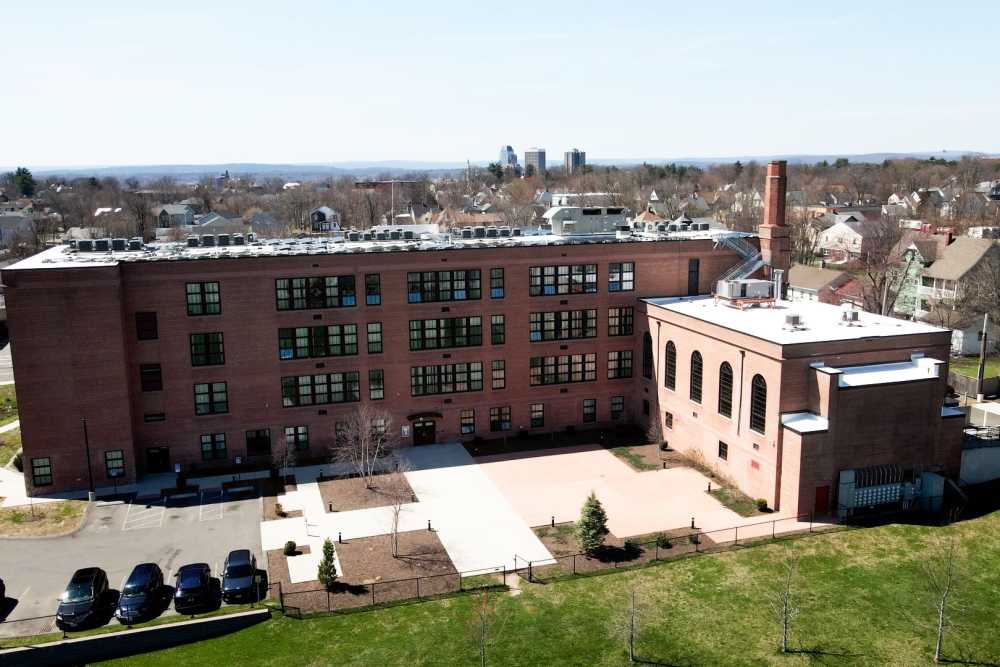 Green lawn with parking lot at building exterior at Elias Brookings Apartments in Springfield, Massachusetts