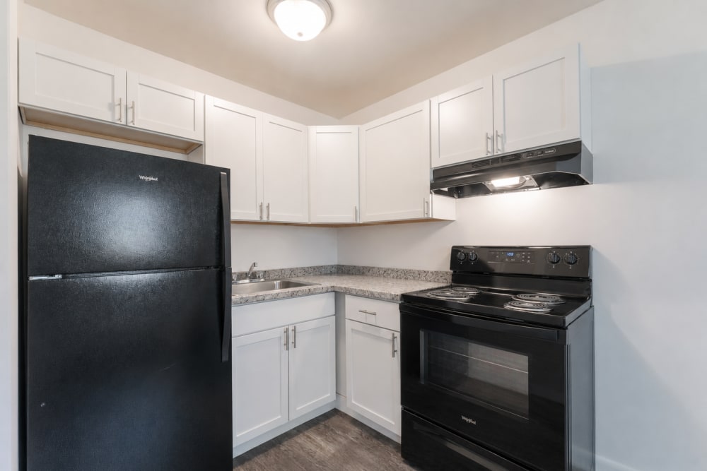 Compact kitchen with white cabinets, black appliances, and corner sink Penfield Village Apartments in Penfield, New York