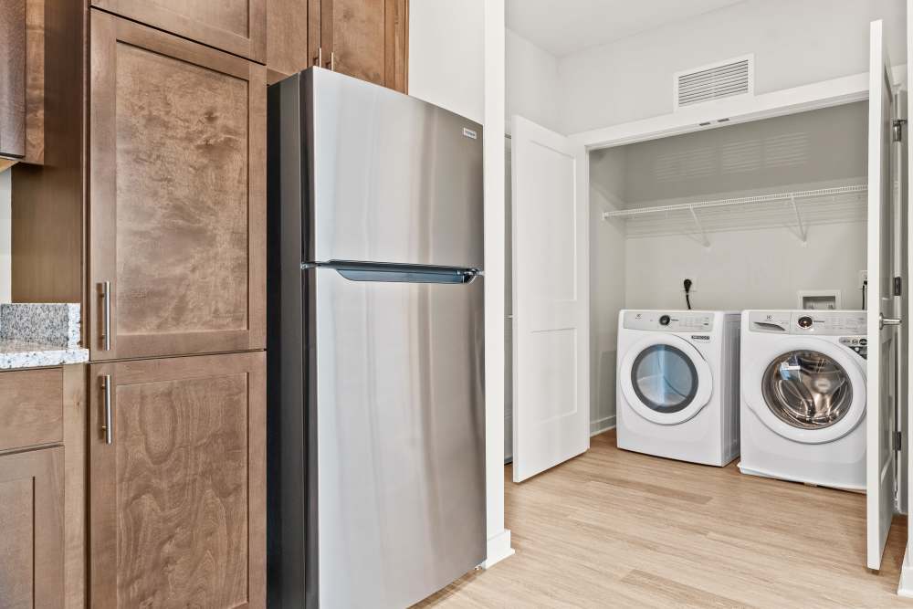 Laundry area with stacked washer and dryer beside stainless steel refrigerator at The Cascade at Foundry Creek in Richmond, Virginia