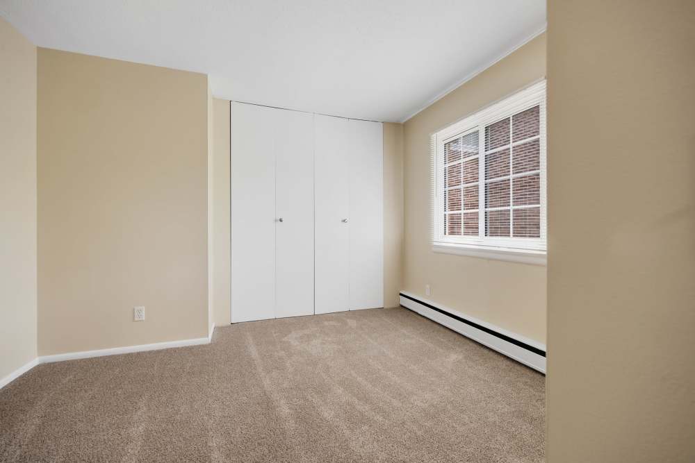Large carpeted bedroom with window and beige walls at Pittsford Village Estates in Pittsford, New York