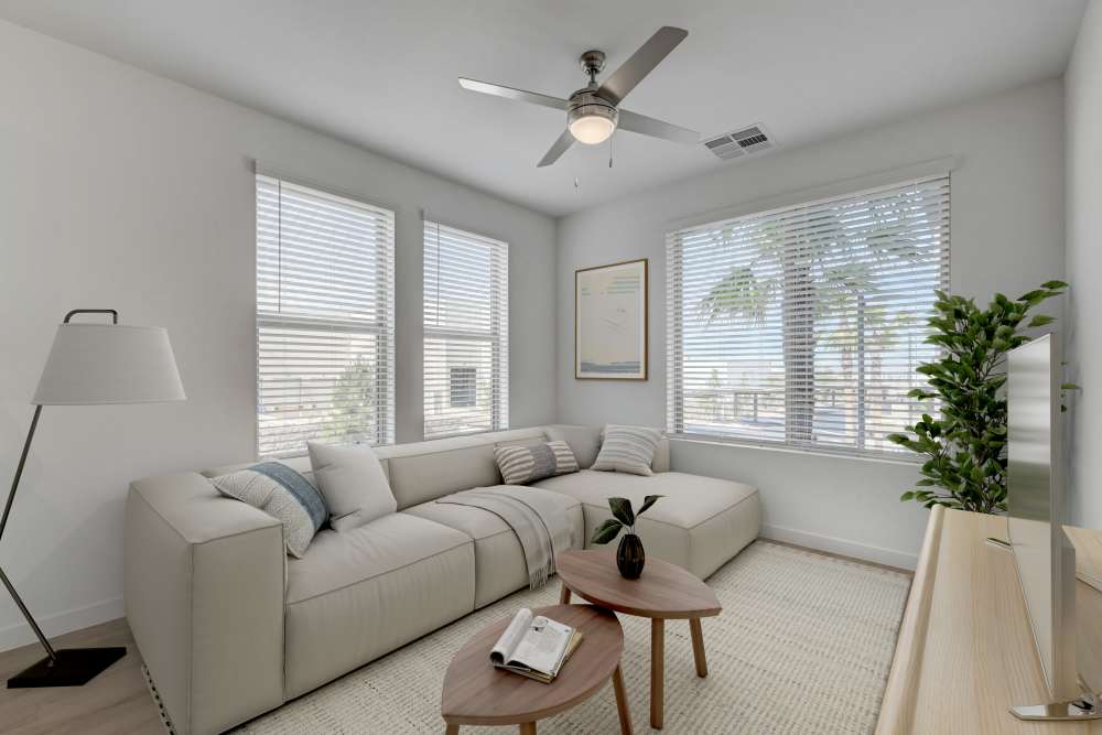 Living room with sectional sofa, ceiling fan, and large bright windows at Heirloom at Bruner in Las Vegas, Nevada