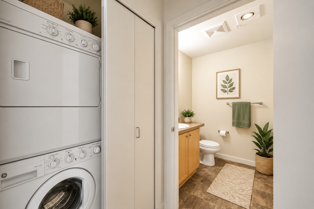 In-unit laundry area with stacked washer and dryer beside a bright hallway at North Main Village in Milwaukie, Oregon  