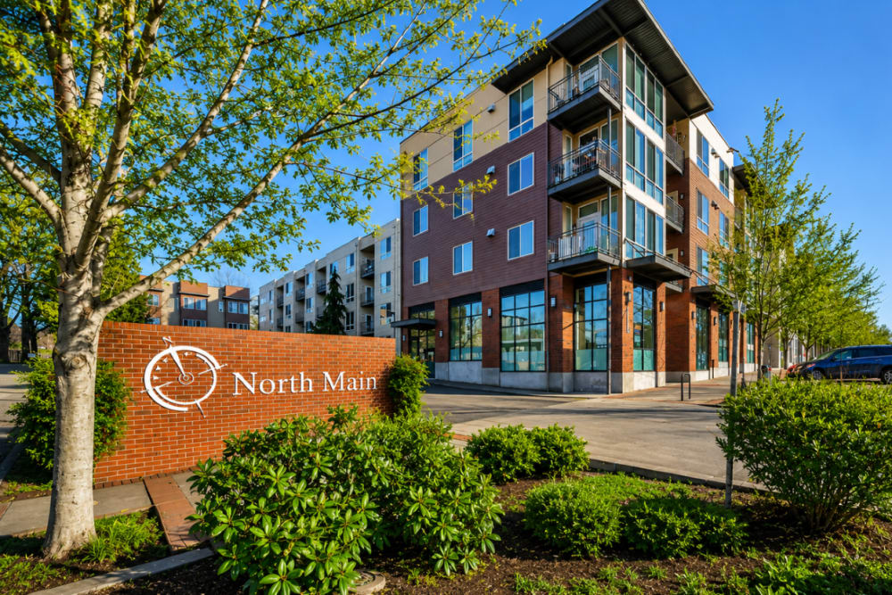 Exterior view of a contemporary apartment community with landscaped grounds and leasing signage at North Main Village in Milwaukie, Oregon  
