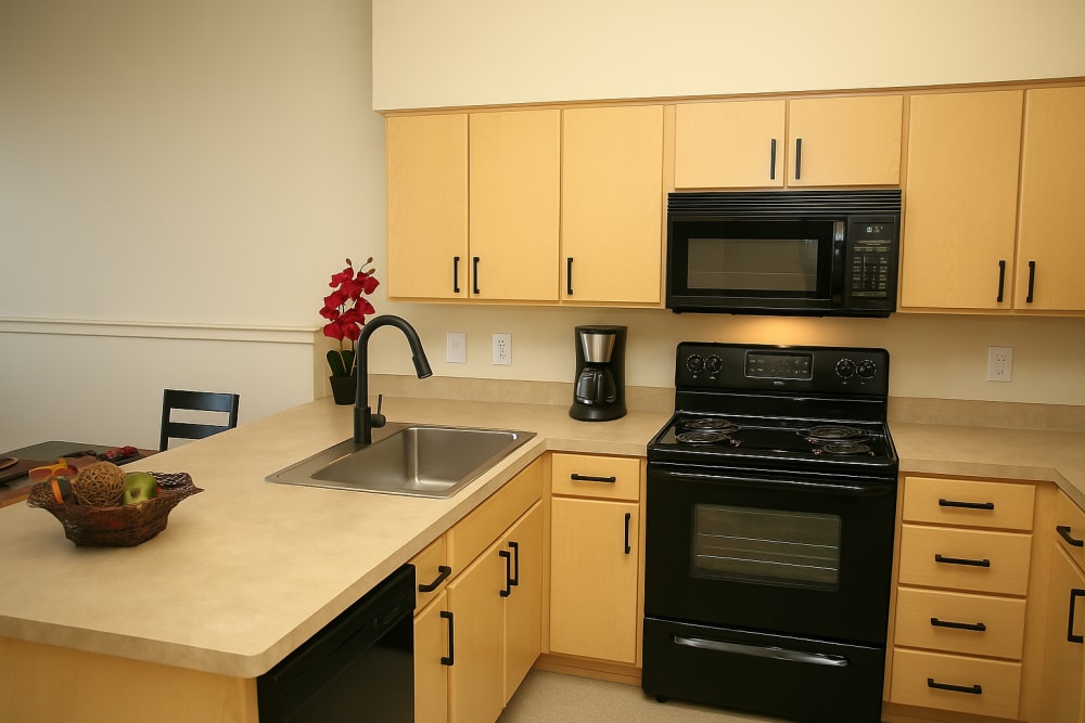 Apartment kitchen with breakfast bar, wood cabinetry, and black appliances at North Main Village in Milwaukie, Oregon  