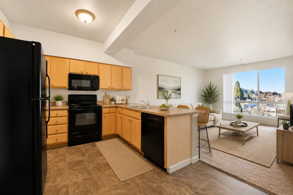 Open-concept apartment kitchen with wood cabinetry, black appliances, and adjacent living space at North Main Village in Milwaukie, Oregon  