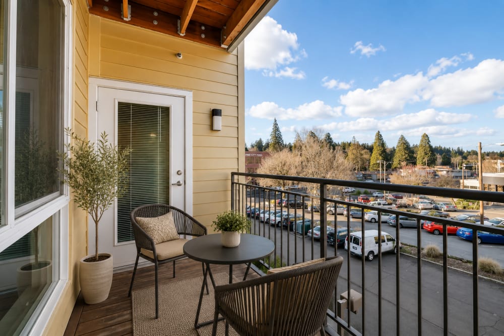 Private apartment balcony with outdoor seating and views of neighboring buildings and landscaped surroundings at North Main Village in Milwaukie, Oregon  