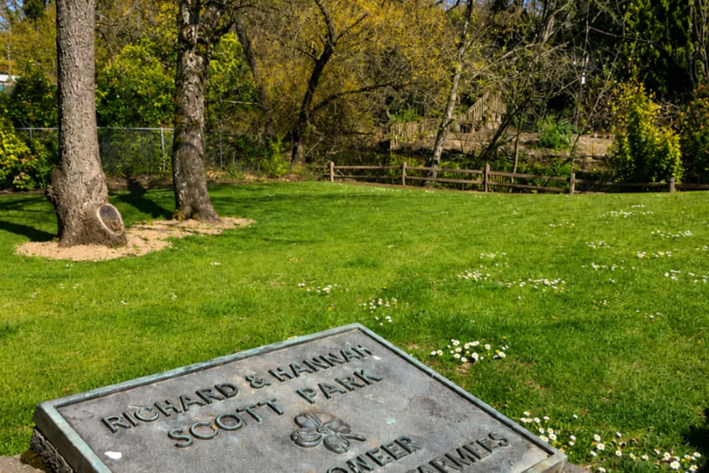 Memorial plaque set in a landscaped green lawn surrounded by mature trees and park-like grounds at North Main Village in Milwaukie, Oregon  