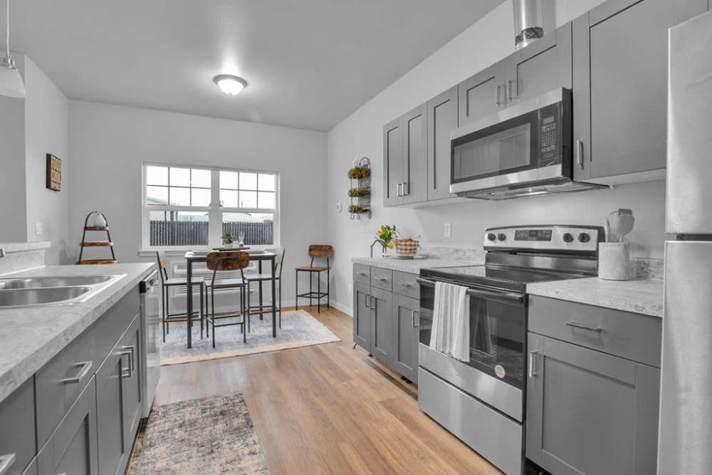 Modern apartment kitchen with gray cabinets, stainless steel appliances, and dining area, at Cleveland Crossings in Woodburn, Oregon
