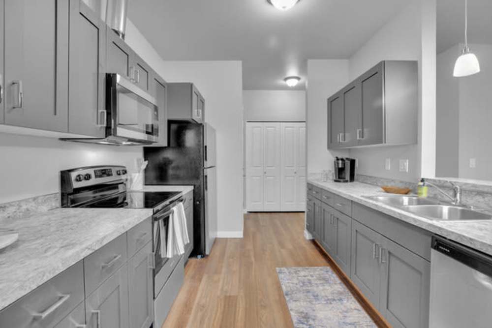 Apartment kitchen featuring gray cabinetry, wood-style flooring, and modern appliances, at Cleveland Crossings in Woodburn, Oregon